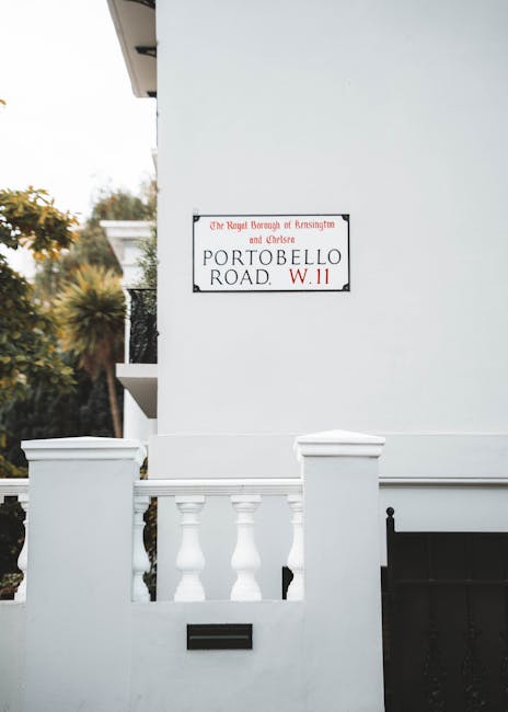 A white exterior wall of a residential property showing a street sign for Portobello Road, W.11, mounted on the wall near the corner of the building. In front of the wall, there is a small white balus