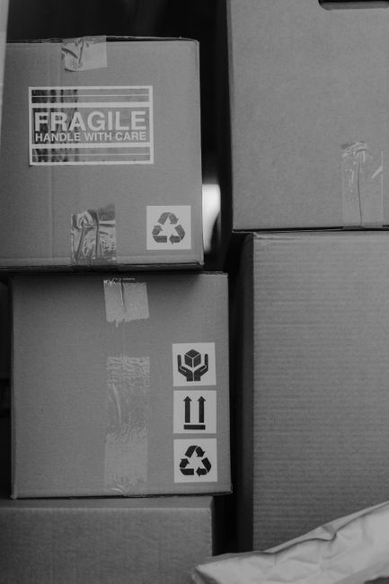 A stack of three cardboard boxes sealed with packing tape, positioned on a floor or staging area within a property. The top box displays a large 'FRAGILE' label with handling instructions, along with 