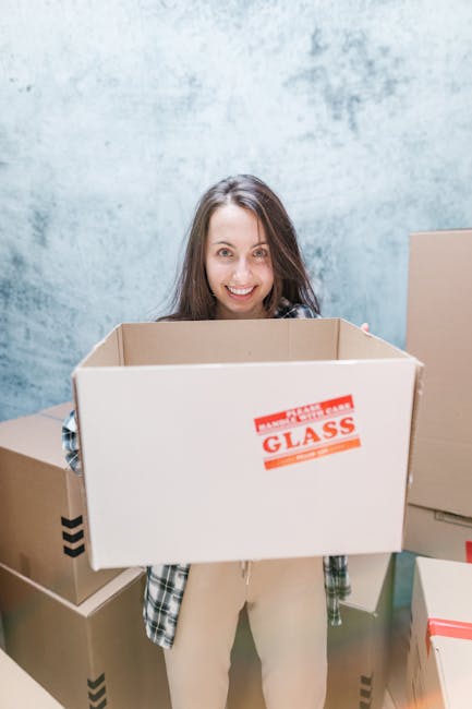 A stack of three cardboard boxes sealed with packing tape, positioned on a floor or staging area within a property. The top box displays a large 'FRAGILE' label with handling instructions, along with 